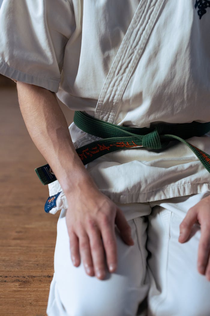 Close-up of a martial artist kneeling in a karate gi with a green belt, focusing on hands and uniform details.